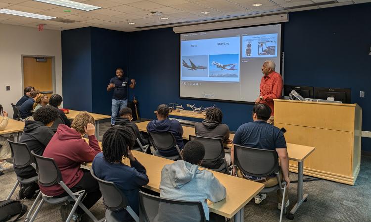 Capt. Tony Holder talks about his career in front of a classroom of students. His presentation on screen shows several photos of airplanes.