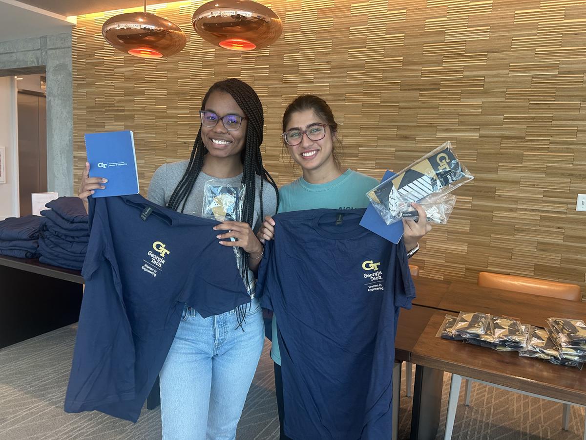 Two students holding WIE T-shirts and other swag